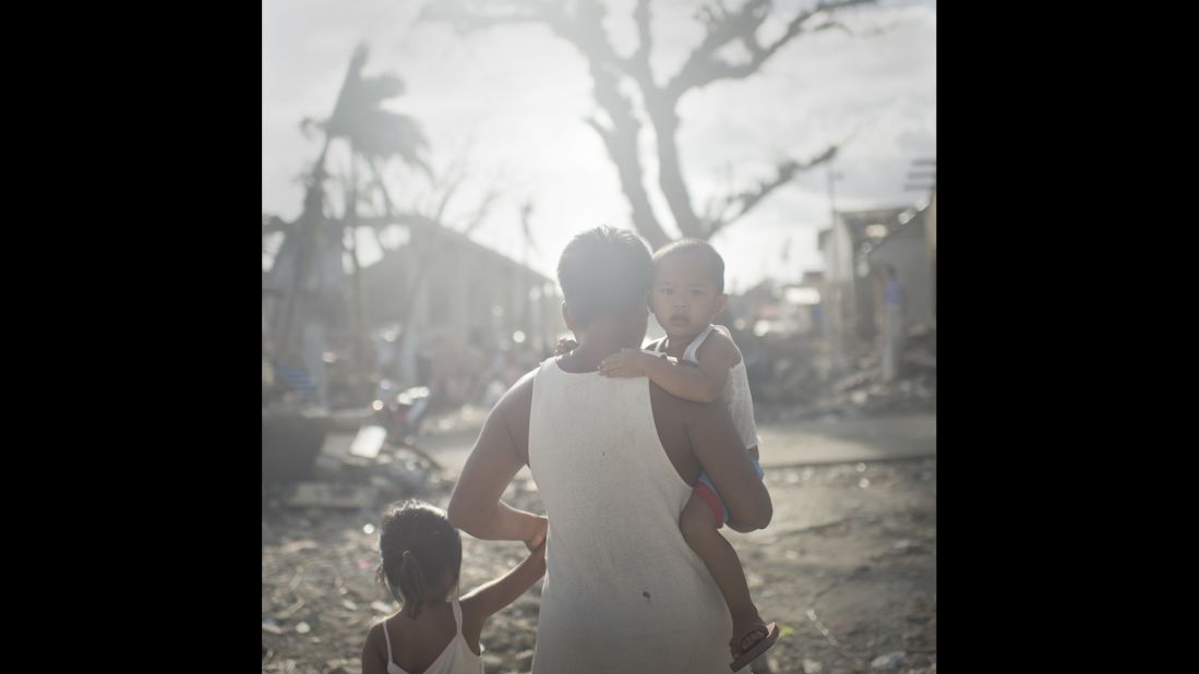 A father walks with his children through the village of San Antonio in Western Samar. The little fishing village was crushed by the storm surge after Haiyan and the majority of the inhabitants lost their homes. During times of disaster the vulnerability of children to illnesses, accidents and violence increases. In San Antonio, 50 people died and bodies were still found a month after the typhoon.  San Antonio, December 2013.