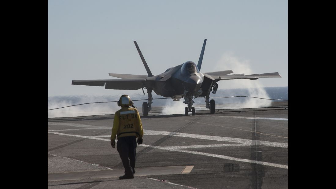 An F-35C jet lands on the deck of the USS Nimitz. To stop, the jet uses a tailhook to grab a wire stretched across the aircraft carrier's deck.