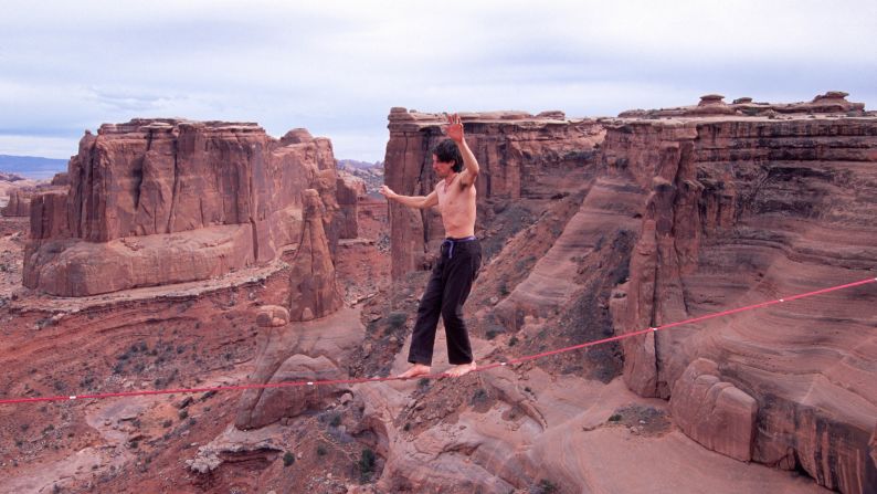 Dean Potter camina a una gran altura en Three Gossips en el Parque Nacional Arches de Utah. A diferencia de caminar sobre la cuerda floja, los equilibristas deben caminar sobre una cuerda suelta en lugar de una que haya sido tensada. Potter ha completado una serie de hazañas practicando este deporte de equilibrio sin equipo de seguridad.