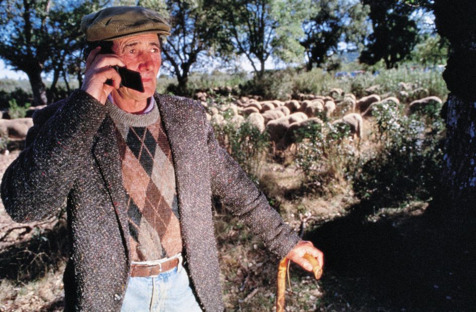 In this 1995 image, a shepherd chats on a flip phone while looking after his flock.