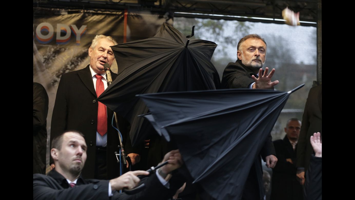 Security personnel use umbrellas to cover Czech Republic President Milos Zeman, top left, during a speech Monday, November 17, in Prague, Czech Republic. During the speech, which commemorated the 1989 Velvet Revolution, protesters booed Zeman and threw objects such as sandwiches, tomatoes and eggs.