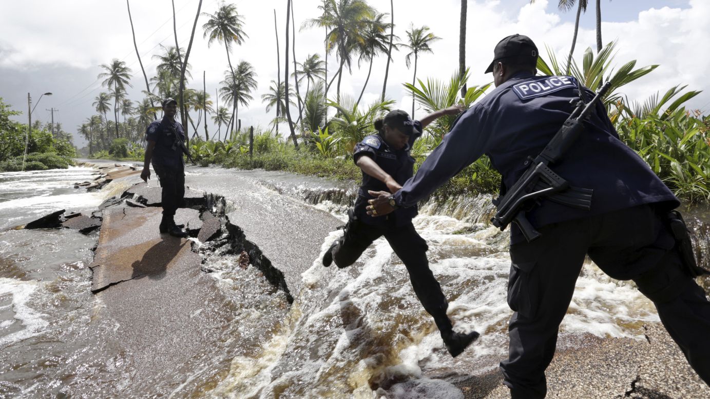 Police Constable Patrice Clarke jumps over a collapsed portion of Manzanilla Mayaro Road as floodwaters continued to flow from the adjoining Nariva swamp Monday, November 17, in Manzanilla, Trinidad.