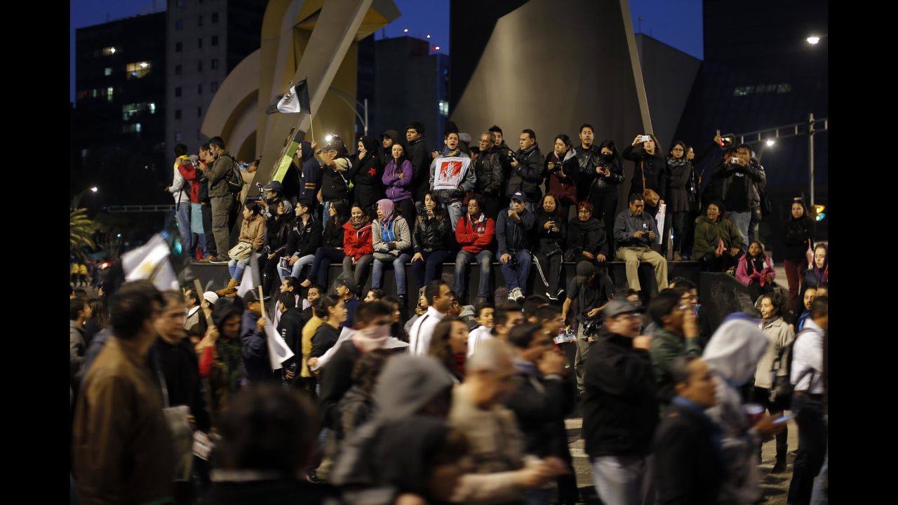 People on the base of a monument watch and cheer on marchers in Mexico City on November 20.