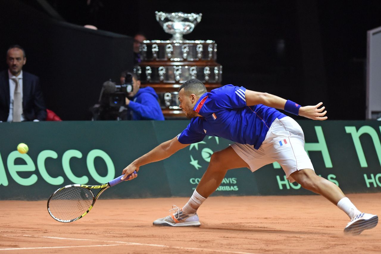 With the giant Davis Cup trophy behind him,  Tsonga stretches to retrieve a shot in going down to Wawrinka