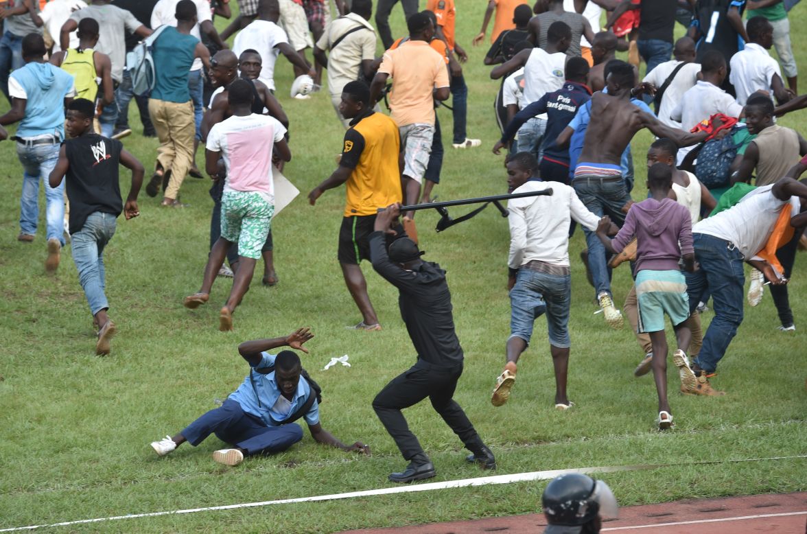 A police officer beats a man in Abidjan, Ivory Coast, as people run on the field following a soccer match between Ivory Coast and Cameroon on Wednesday, November 19. The 0-0 draw clinched a place for both countries in next year's Africa Cup of Nations.  
