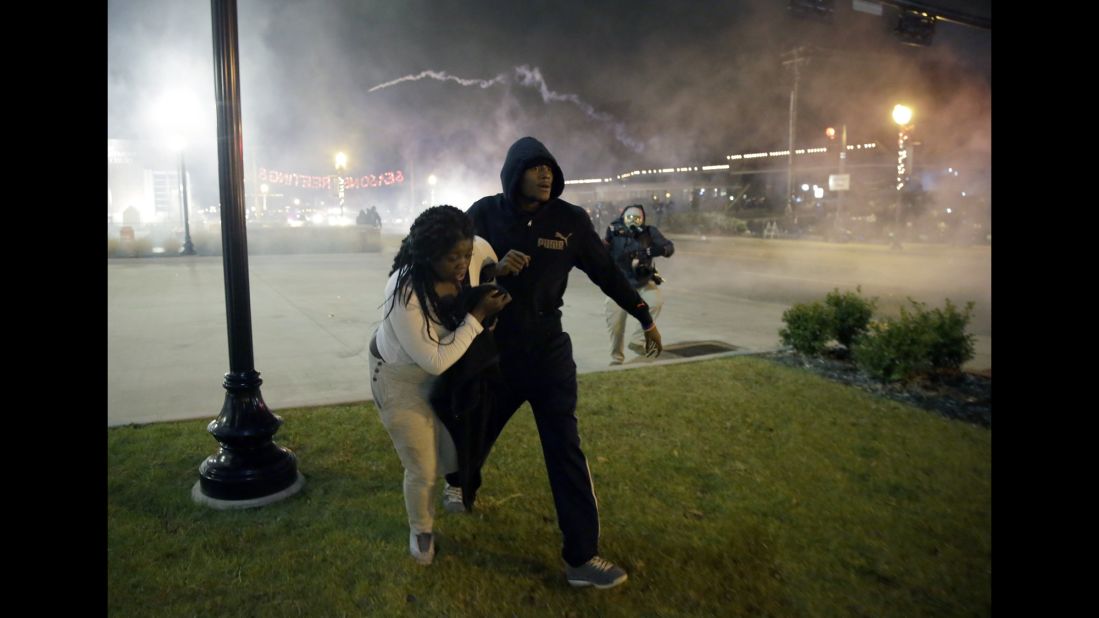 Protesters run for shelter as smoke fills the streets of Ferguson on November 24.