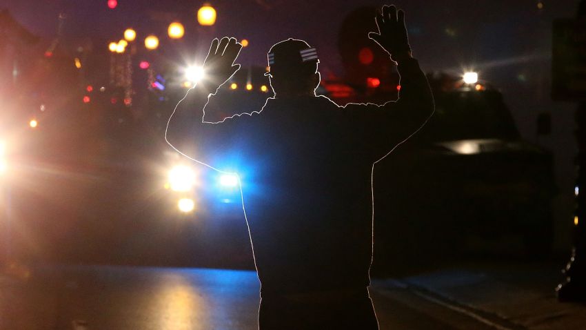 A protestor stands in front of police vehicles with his hands up in Ferguson.
