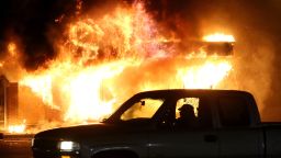 Caption:FERGUSON, MO - NOVEMBER 25: A car drives by a burning building during a demonstration on November 25, 2014 in Ferguson, Missouri. Ferguson has been struggling to return to normal after Brown, an 18-year-old black man, was killed by Darren Wilson, a white Ferguson police officer, on August 9. His death has sparked months of sometimes violent protests in Ferguson. A grand jury today declined to indict officer Wilson. (Photo by Justin Sullivan/Getty Images)