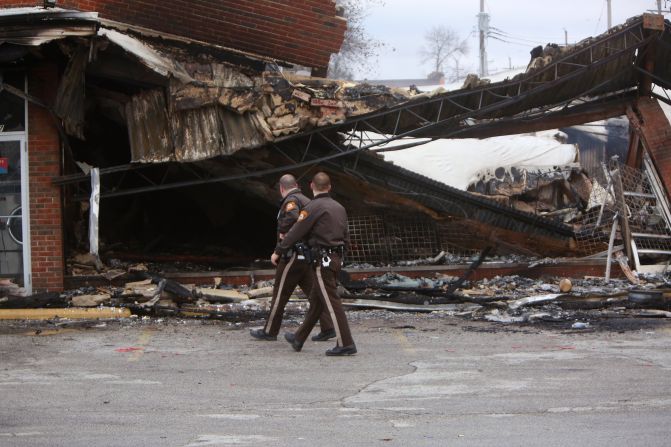 Police officers walk past the smoldering remains of a beauty supply store in Ferguson, Missouri, on Tuesday, November 25. Ferguson has been struggling to return to normal since Michael Brown, an unarmed black teenager, was killed by Darren Wilson, a white police officer, on August 9. The grand jury did not indict Wilson in the case, prompting new waves of protests in Ferguson and <a href="index.php?page=&url=http%3A%2F%2Fwww.cnn.com%2F2014%2F11%2F25%2Fjustice%2Fgallery%2Fnational-ferguson-protests%2Findex.html">across the country.</a>