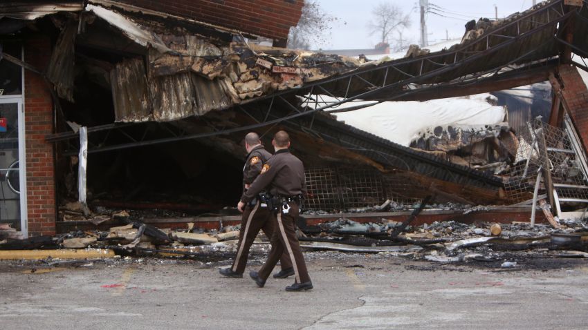 Police officers walk past the smoldering remains of a beauty supply store in Ferguson on Tuesday, November 25.