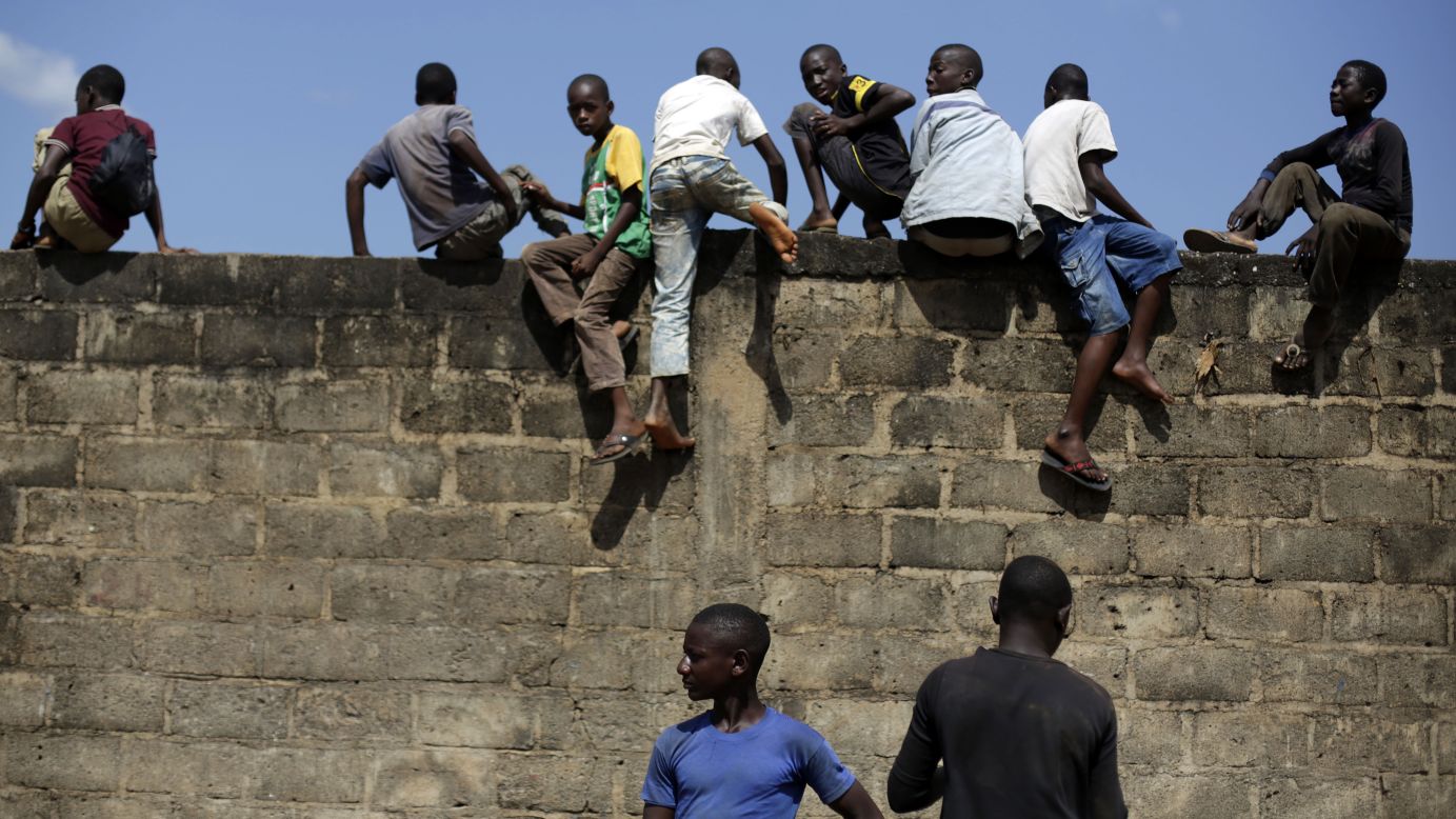 Children climb a wall to see a helicopter land in Gueckedou, Guinea, on Friday, November 21.