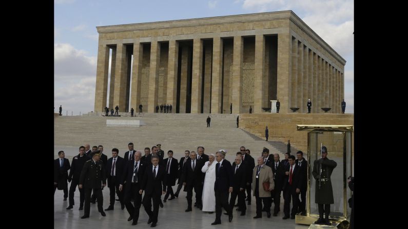 The Pope, surrounded by security and officials, walks the grounds of the mausoleum November 28.