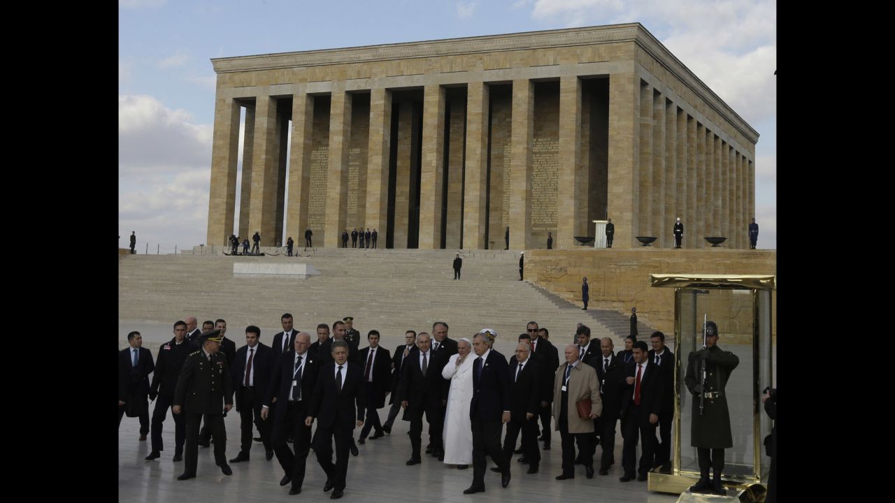 The Pope, surrounded by security and officials, walks the grounds of the mausoleum November 28.