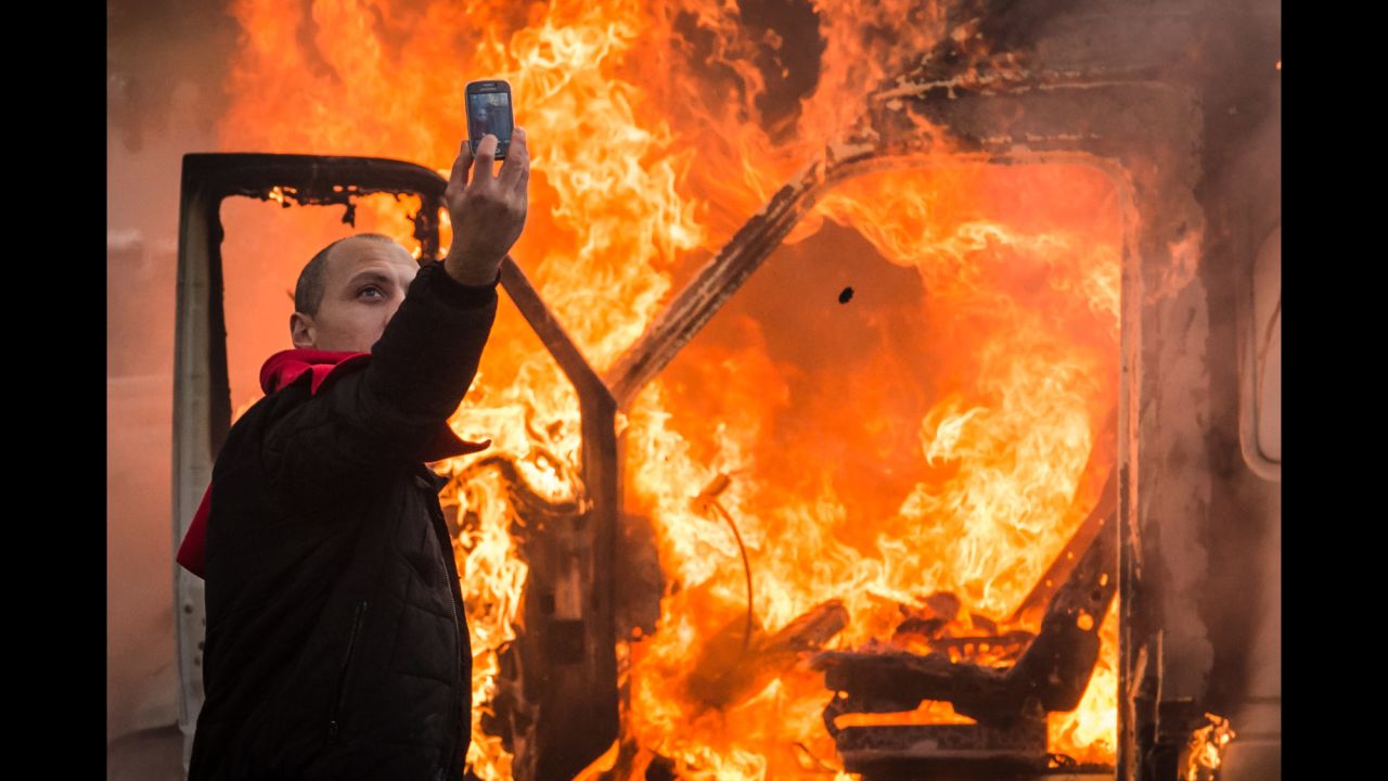 A protester takes a selfie in front of a burning car in Brussels, Belgium, on Thursday, November 6. Tens of thousands of demonstrators converged on the Belgian capital to protest government policies that would extend the pension age, contain wages and cut into public services.
