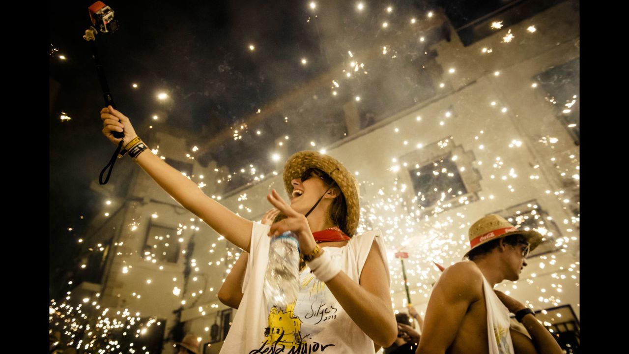 A girl takes a selfie in front of people setting off fireworks during a festival in Sitges, Spain, on Saturday, August 23.