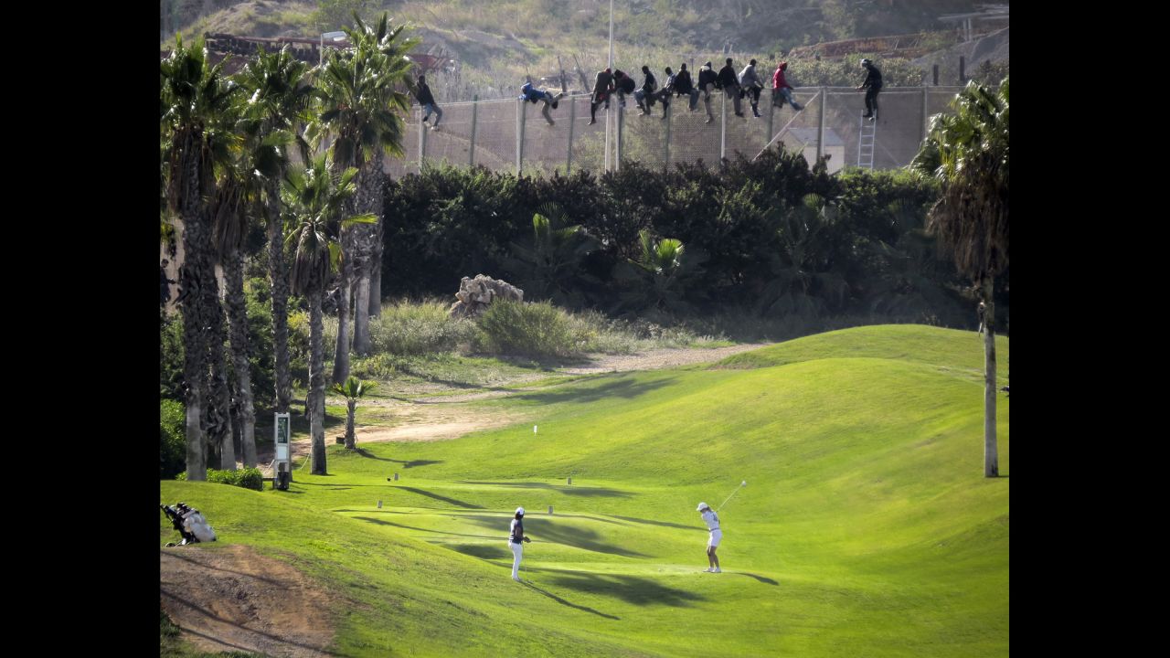 <strong>October 22:</strong> A golfer hits a tee shot as African migrants sit atop a border fence dividing Morocco and the Spanish enclave of Melilla.