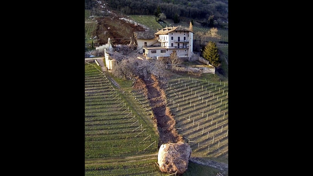 <strong>January 23:</strong> A trail of destruction is seen behind a boulder after a landslide in Ronchi di Termeno, Italy. The boulder missed the farmhouse at right but destroyed a barn before stopping in a vineyard. According to reports, the family living at the house was unharmed.