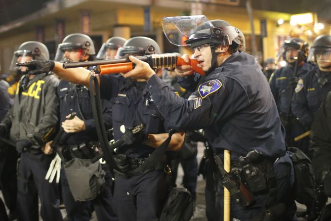 A police officer raises a shotgun toward the crowd in Berkeley on Saturday, December 6.