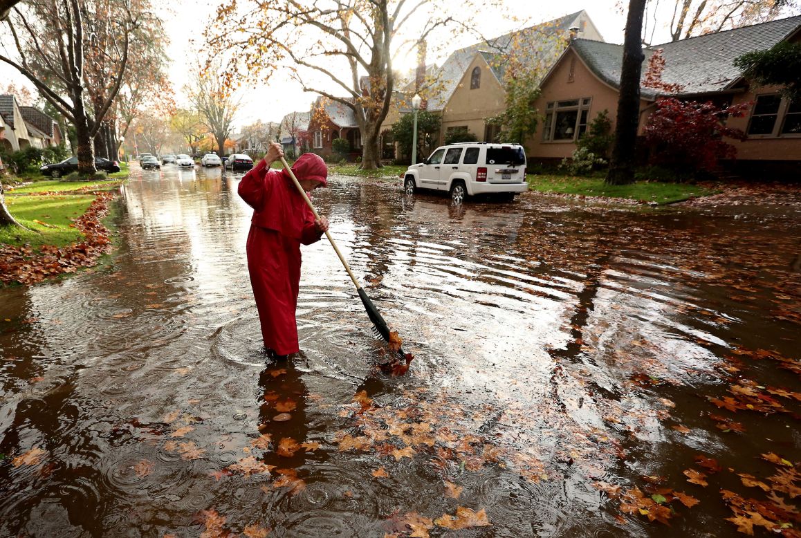 A woman stands in knee-deep water as she clears a clogged storm drain that had caused her street to flood in Sacramento, California, on Wednesday, December 3.