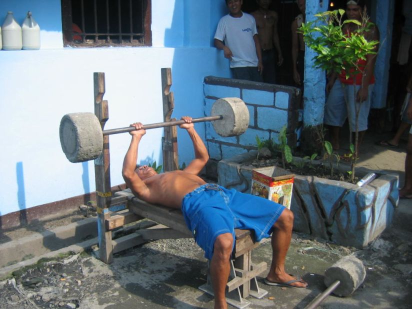 Ninety-five percent of inmates of NBP belong to 12 gangs, according to research by Clarke Jones and Raymund Narag, who took these images in the summer of 2012. Gang culture within the prison often leads to violence, but they say it also fills an important void. Here a prisoner is seen exercising using improvised weights.