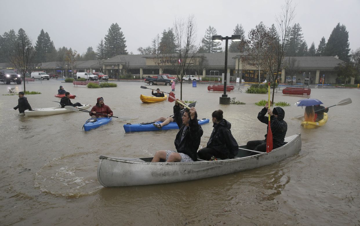 People in kayaks and a canoe make their way around a flooded parking lot at a shopping center on Thursday, December 11, in Healdsburg, California. 