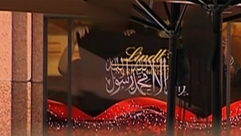 Hostages behind the cafe's window hold up a black flag with Arabic script on December 15.