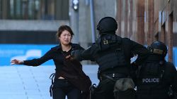 A hostage runs to armed tactical response police officers for safety after she escaped from a cafe under siege at Martin Place in the central business district of Sydney, Australia, Monday, Dec. 15, 2014. New South Wales state police would not say what was happening inside the cafe or whether hostages were being held. But television footage shot through the cafe's windows showed several people with their arms in the air. (AP Photo/Rob Griffith)