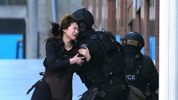 A hostage runs to armed tactical response police officers for safety after she escaped from a cafe under siege at Martin Place in the central business district of Sydney, Australia, Monday, Dec. 15, 2014. New South Wales state police would not say what was happening inside the cafe or whether hostages were being held. But television footage shot through the cafe's windows showed several people with their arms in the air. (AP Photo/Rob Griffith)