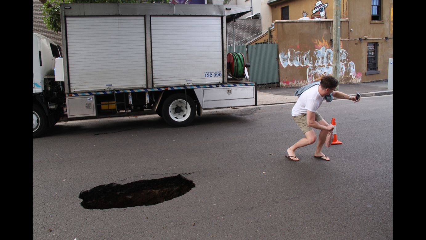 A man squats to get a picture with a sinkhole in Sydney on Saturday, December 13.