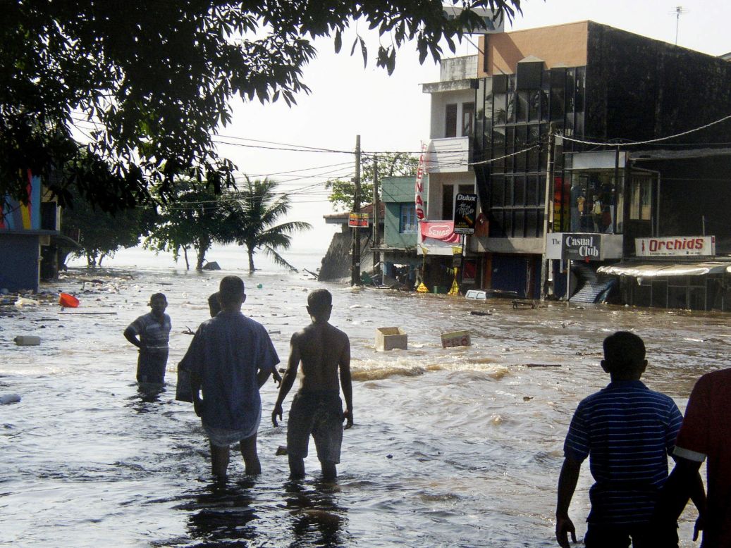 Sri Lankan pedestrians walk through floodwaters in a main street in Galle, after the coastal town was hit by a tidal wave.