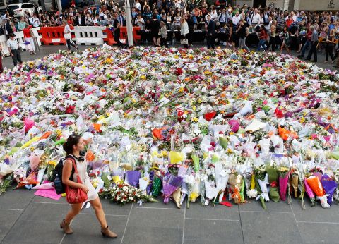 A woman walks past flowers placed by people as a mark of respect for the victims of Martin Place siege on Tuesday, December 16.
