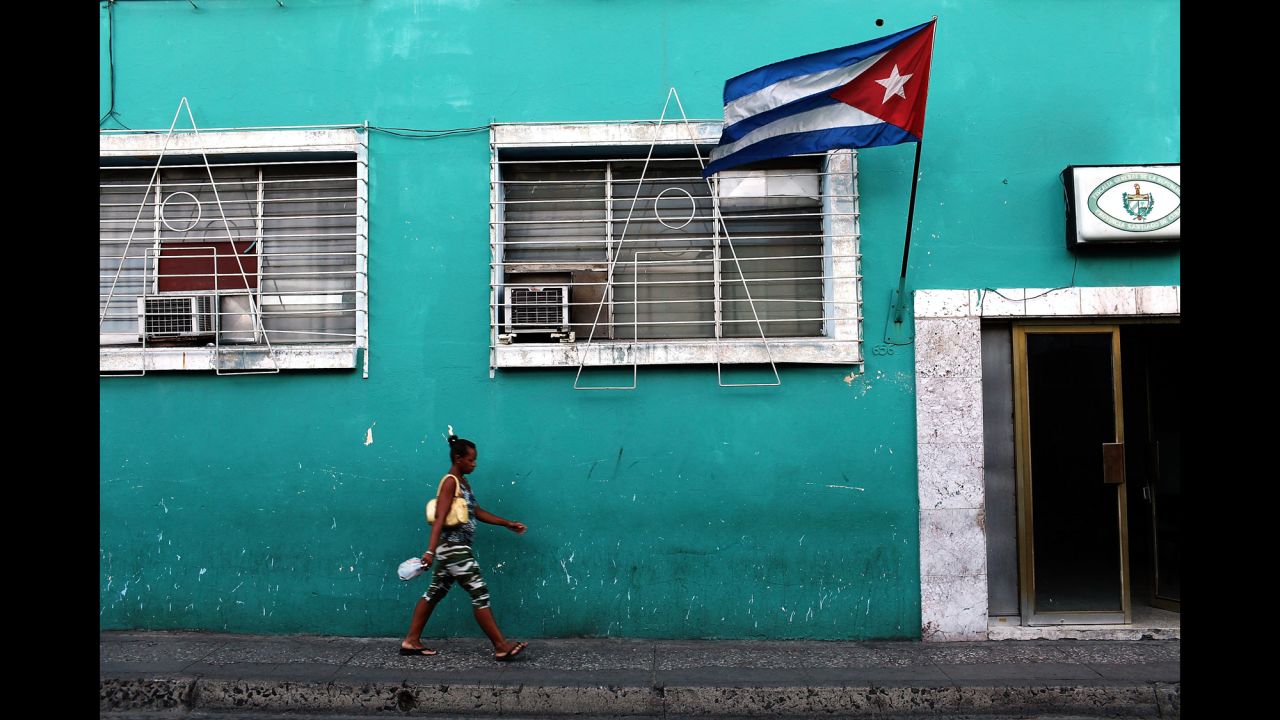 A woman walks under a Cuban flag in Santiago de Cuba, Cuba, in March 2012.