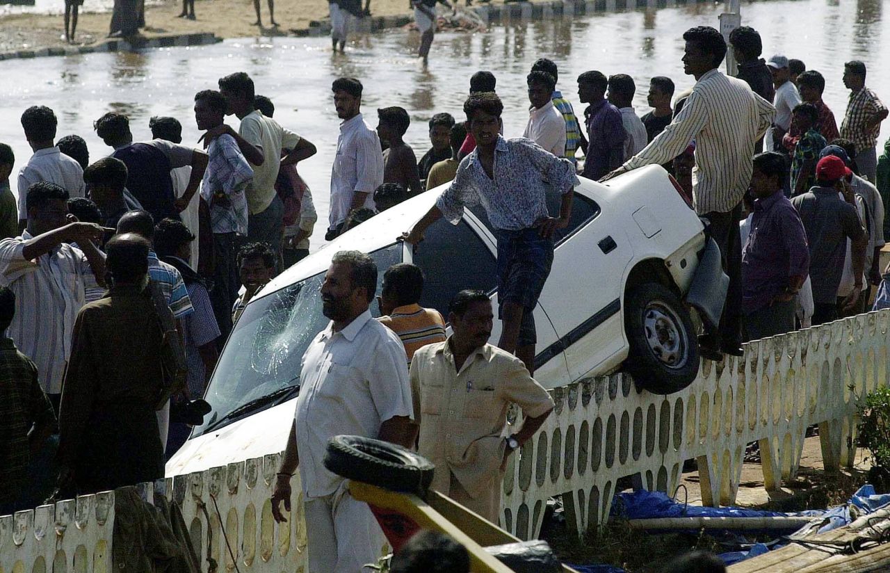 Bystanders watch rescue operations at Marina Beach in Chennai on December 26, 2004. Powerful waves sent this car crashing onto a road barrier. 