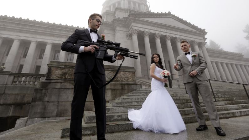 The best man in a wedding party holds an AR-10 rifle while the party was having its pre-wedding portraits taken on the steps of the state capitol in Olympia, Washington, on Saturday, December 13. The man was handed the gun by activist Brandon Lyons, who was participating in a protest against the state's new law that requires background checks on all gun sales and transfers, including private transactions. The wedding party, which declined to be identified, was not part of the protest.