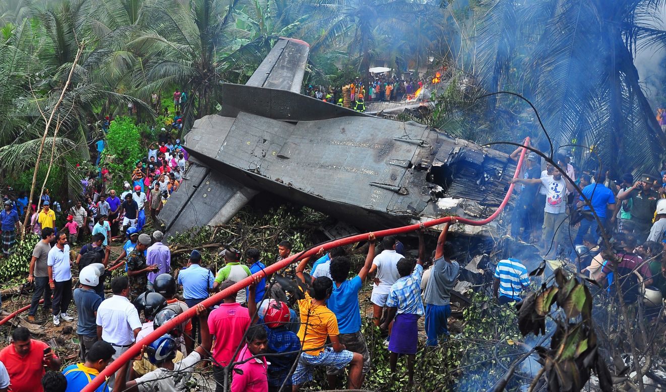 People gather around a downed aircraft in Athurugiriya, Sri Lanka, as firefighters try to extinguish flames amid the debris on Friday, December 12. The Sri Lanka Air Force plane crashed into a rubber plantation, killing all four people on board, police said.