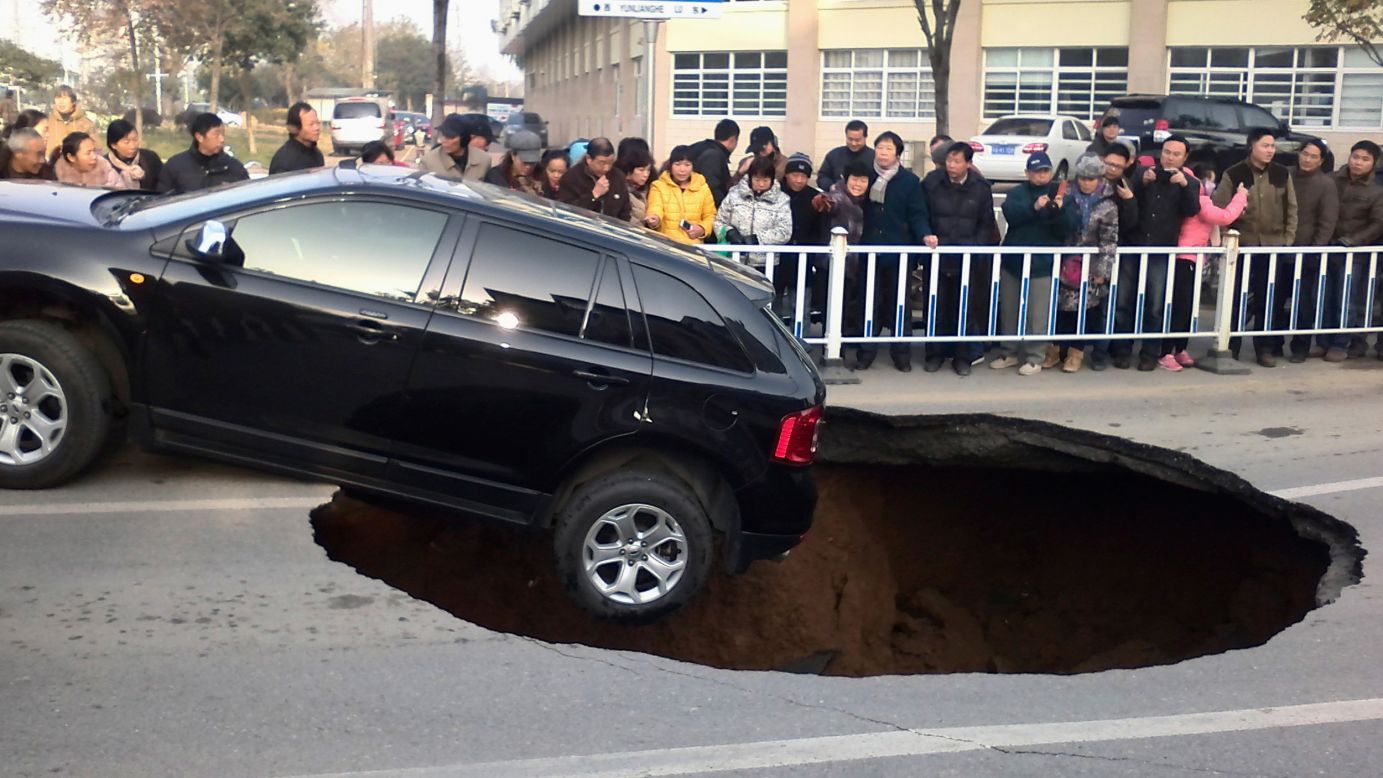 People in Zhenjiang, China, watch a car dangle on the edge of a giant sinkhole on Friday, December 12.