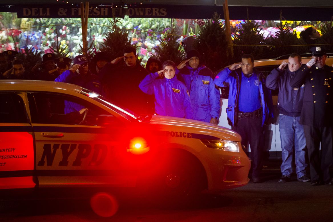 Mourners stand at attention as the bodies of two fallen NYPD officers are transported from Woodhull Medical Center on Saturday, December 20. 