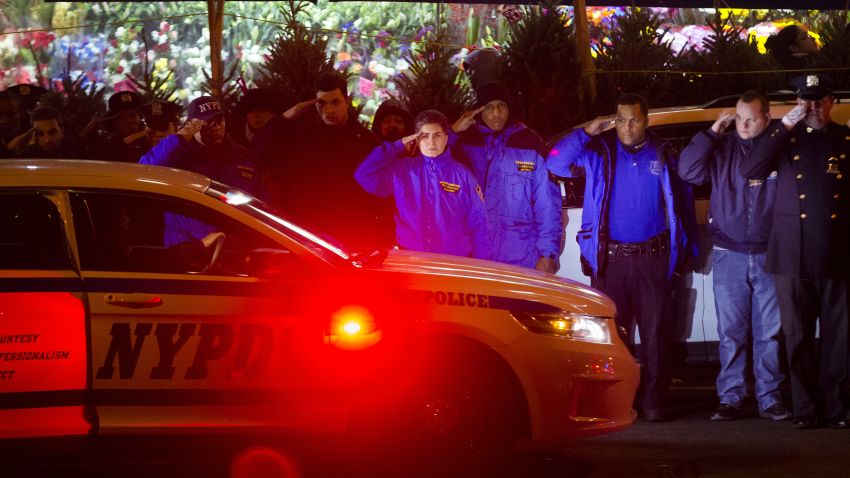 Mourners stand at attention as the bodies of two fallen NYPD police officers are transported from Woodhull Medical Center on Saturday, December 20. 