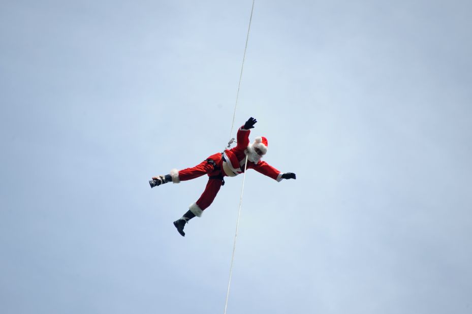Firefighter Hector Chaco maneuvers down a cable from a bridge to deliver presents to children as Santa in Guatemala City.