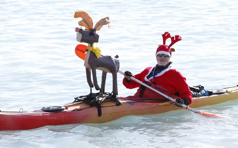 A man in a Santa outfit paddles a canoe decorated with a reindeer during the traditional Christmas bath in Nice, France.