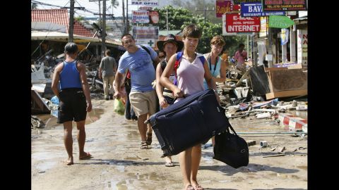 Travelers walk past devastation, carrying their luggage, as they head to the airport on December 27, 2004. Patong Beach was one of the worst hit provinces of Phuket, Thailand. 