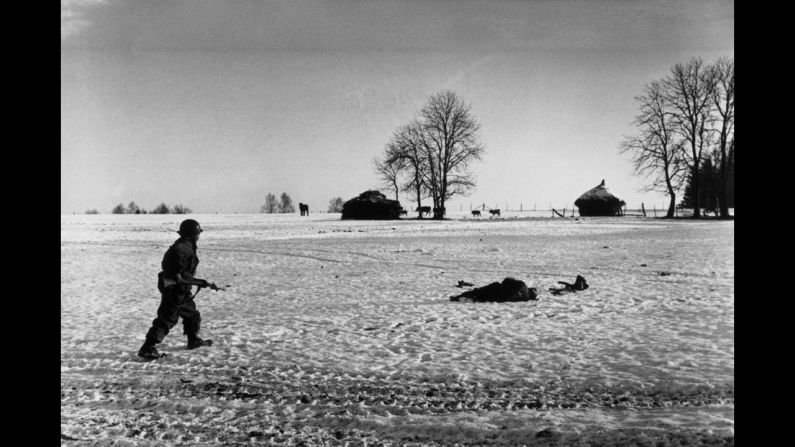 An American soldier walks past a casualty during the Battle of the Bulge.