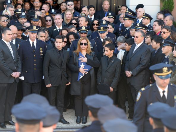 Maritza Ramos, center, wife of Officer Ramos, holds the colors as she is flanked by her sons Justin, left, and Jaden during the funeral service.