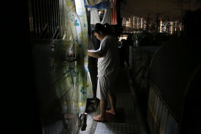 Sze Suk Pui, a migrant who moved from China to Hong Kong three years ago, turns to the light inside the flat to read a free luncheon notice from a church.