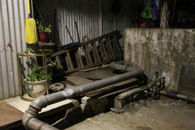 The rooftop houses are connected by dimly lit walkways boarded with wooden planks and cluttered with unwanted household items.