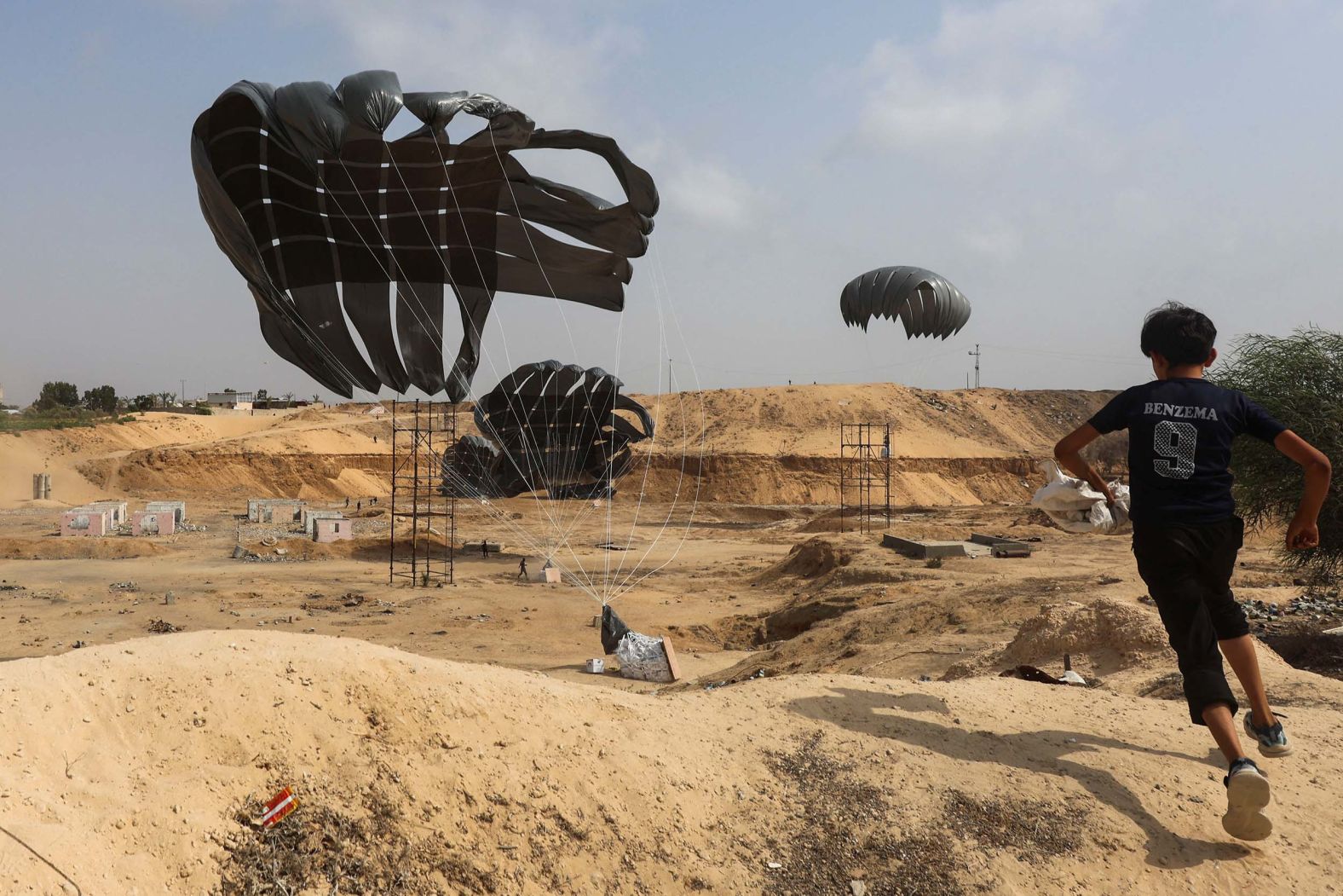 A Palestinian boy runs toward aid packages that were airdropped from a plane in Dier al-Balah, Gaza, on Tuesday, August 12.