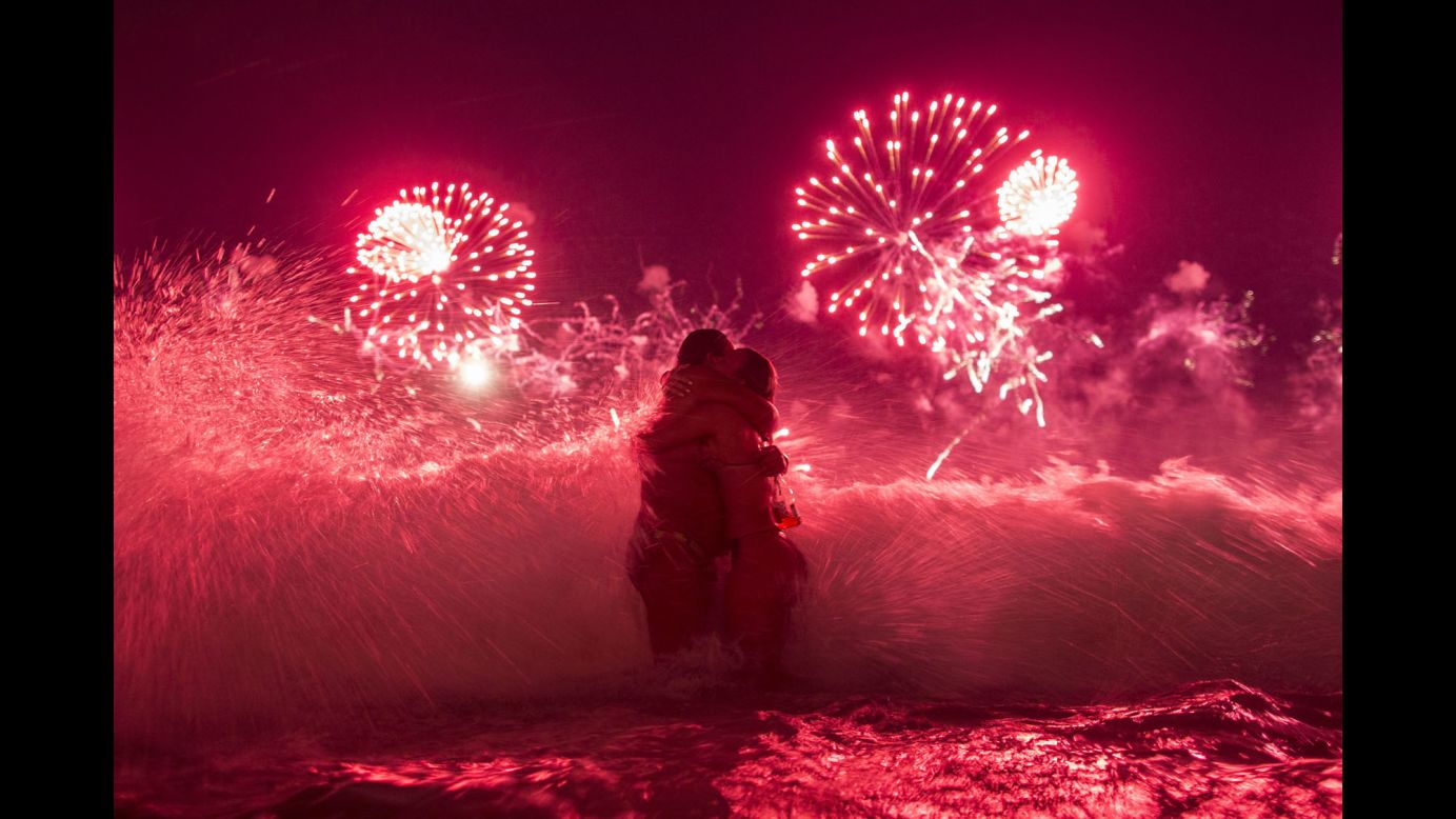 A wave crashes as two women hug and fireworks explode over Copacabana beach in Rio de Janeiro early on Thursday, January 1.
