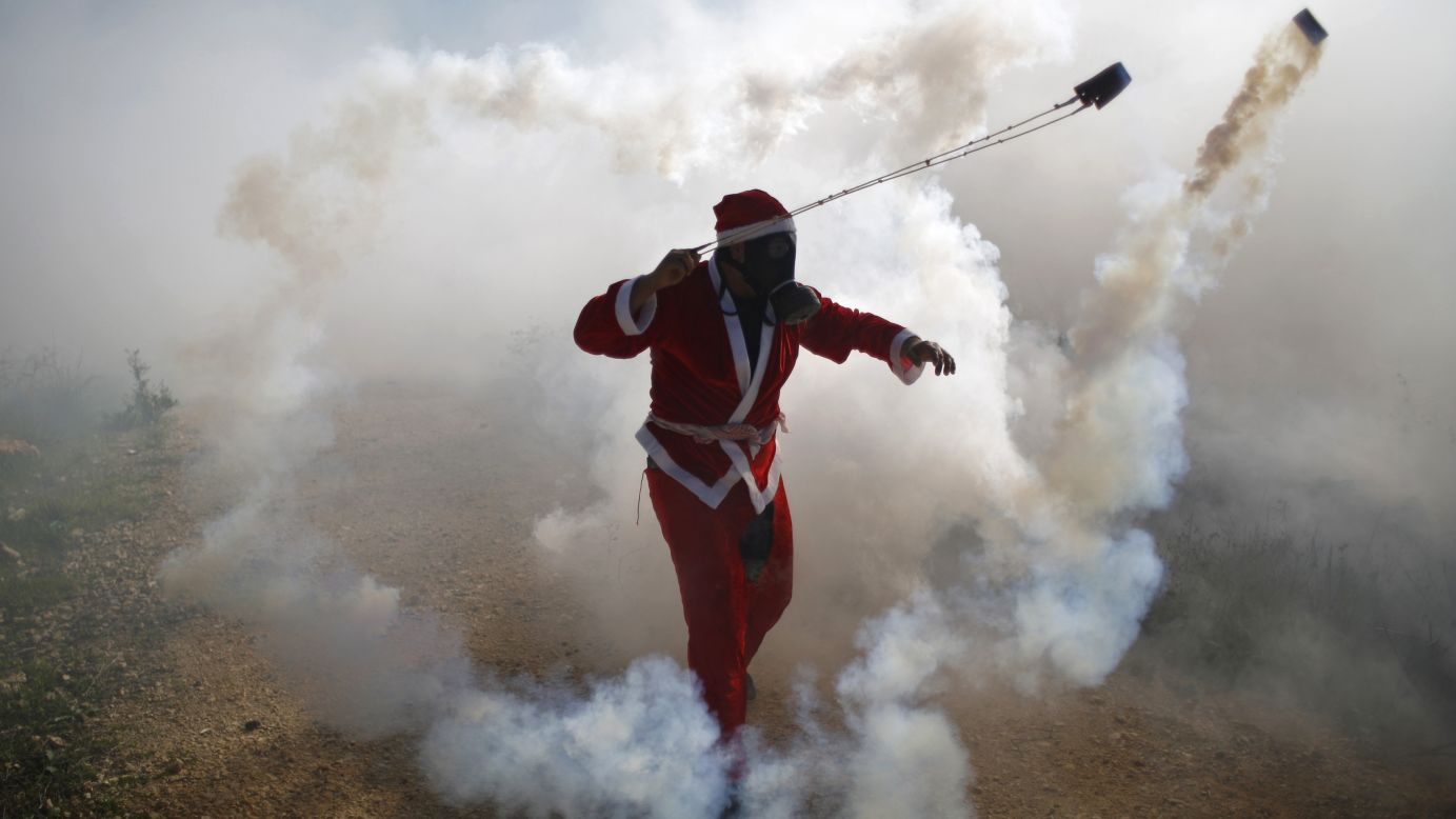A Palestinian protester, dressed as Santa Claus, uses a slingshot to return a tear gas canister fired by Israeli troops during clashes in the West Bank village of Bilin on Friday, December 26.