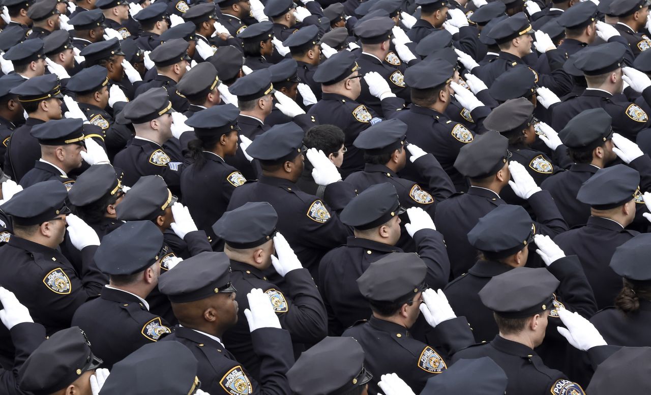 Police officers gathered for the funeral salute the fallen officer.