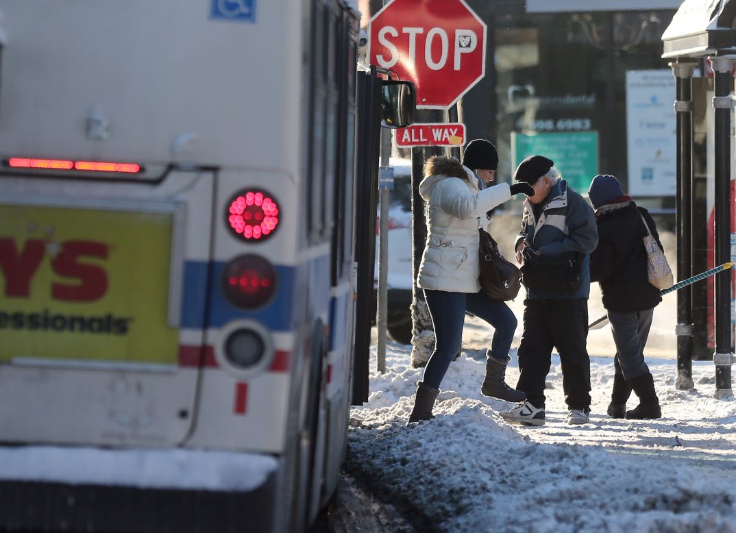 Bus riders step across a snow-piled sidewalk on January 6 in Chicago.